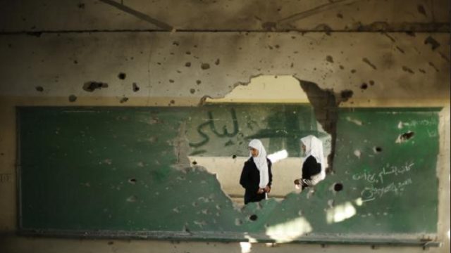 палестинские студенты смотрят на разрушенную стену класса